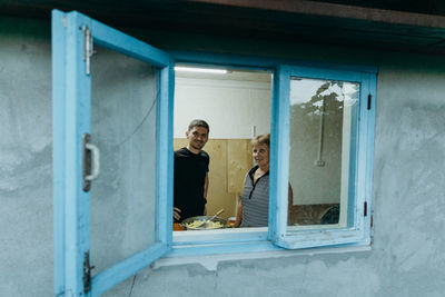 An elderly woman with her grandson is frying potatoes in a frying pan on the stove.