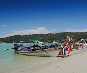 Boats moored on beach against blue sky