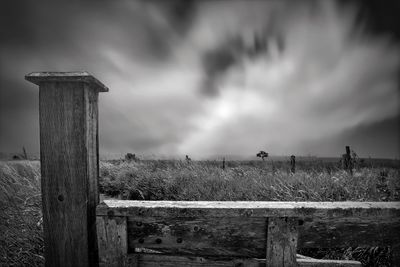 Fence on field against cloudy sky