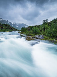 A river surrounded by forest, cascading over rocky rapids and framed by an ethereal sky 