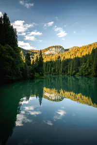 Tranquil landscape at the mountain lake, with the vibrant sky, white clouds, reflected  in the water