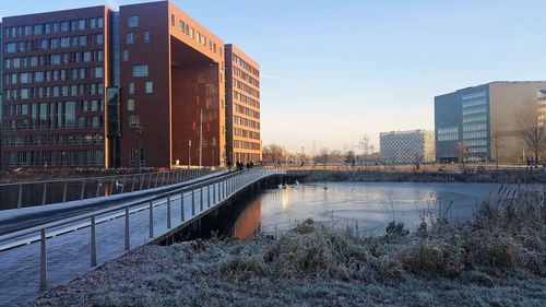 Bridge over canal by buildings against sky during winter