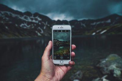 Human hand using mobile phone against mountain