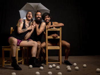 Portrait of young jugglers sitting on chairs with balls and umbrella on stage