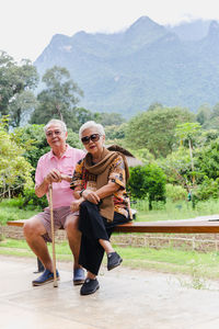 Vertical of asian senior couple sit on a bench on vacation outdoors