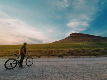 Rear view of man riding bicycle on field against sky