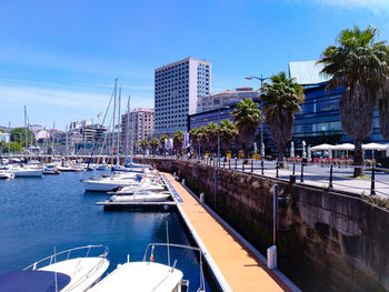 Sailboats moored in river by buildings against blue sky