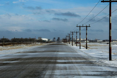 Road by electricity pylon against sky during winter