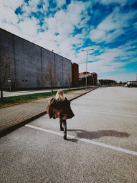 Rear view of woman walking on road against sky in city