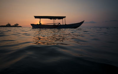 Silhouette person sitting in boat on sea against sky during sunset