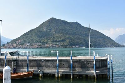 Boats moored on sea by mountains against clear sky