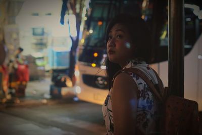 Young woman looking away while standing on street in city