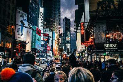 People walking on city street against illuminated buildings