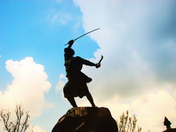 Low angle view of silhouette man standing on rock against sky