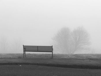 Empty bench on field against sky