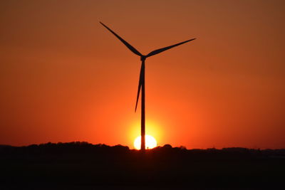 Silhouette wind turbines on field against sky during sunset