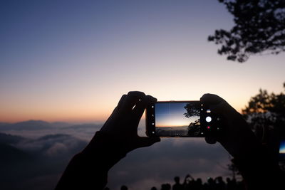 Close-up of hands holding mobile phone photographing sunset