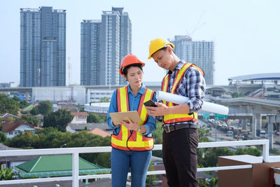 Engineers using mobile phone while standing against buildings in city