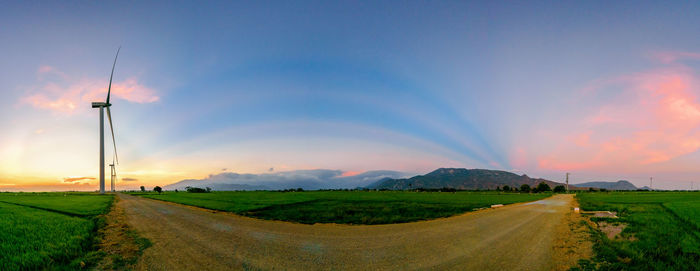 Road by agricultural field against sky during sunset