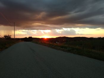 Road amidst landscape against dramatic sky during sunset