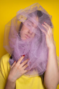 Close-up of young woman standing against yellow background