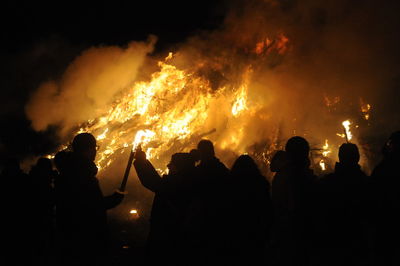 Silhouette people by fire against sky at night