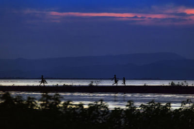 Silhouette people on beach against sky during sunset