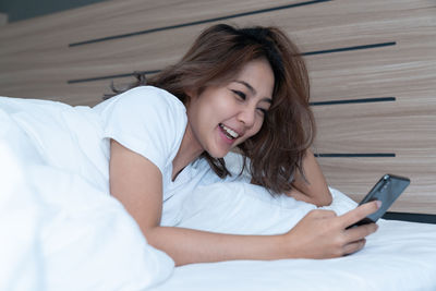 Young woman using mobile phone while relaxing on bed