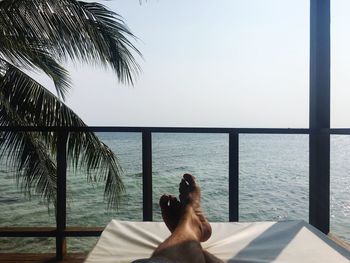 Low section of woman relaxing on sea shore against clear sky