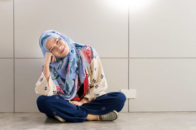 Portrait of smiling young woman wearing hijab sitting on tiled floor