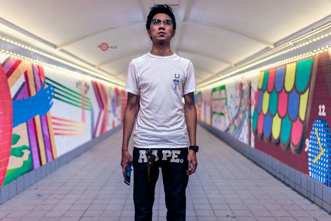indoors, casual clothing, lifestyles, looking at camera, front view, full length, person, portrait, standing, leisure activity, young adult, three quarter length, architecture, built structure, graffiti, wall - building feature, smiling