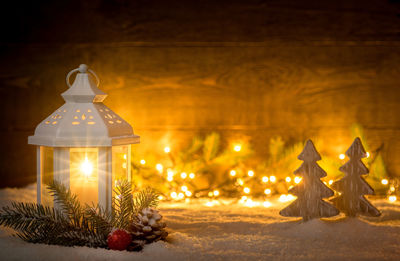 Close-up of illuminated lantern by christmas decorations on snow