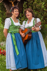 Women singing while standing on grassy field against tree