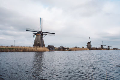 Traditional windmill by river against sky