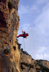 Side view of man climbing mountain against sky