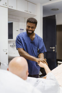 Smiling male nurse holding hands of senior patient lying on bed in hospital