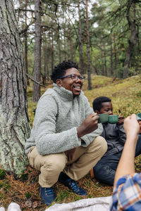 Happy father holding cup while crouching with family in forest