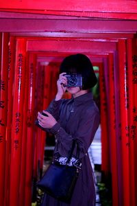 Full length of young woman standing against red wall torii gate 