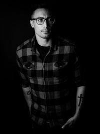 Portrait of young man standing against black background