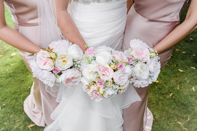 Midsection of bride and bridesmaids holding bouquets while standing on field