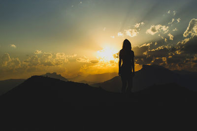 Rear view of silhouette woman standing against sky during sunset