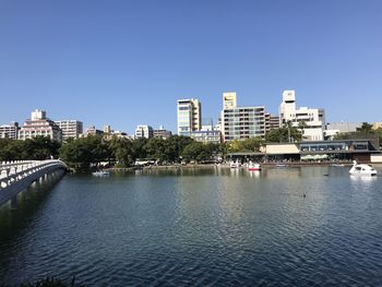 Buildings by river against clear blue sky