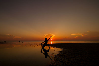 Silhouette woman doing yoga at beach against sky during sunset