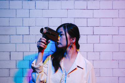 Young woman filming through video camera in front of wall