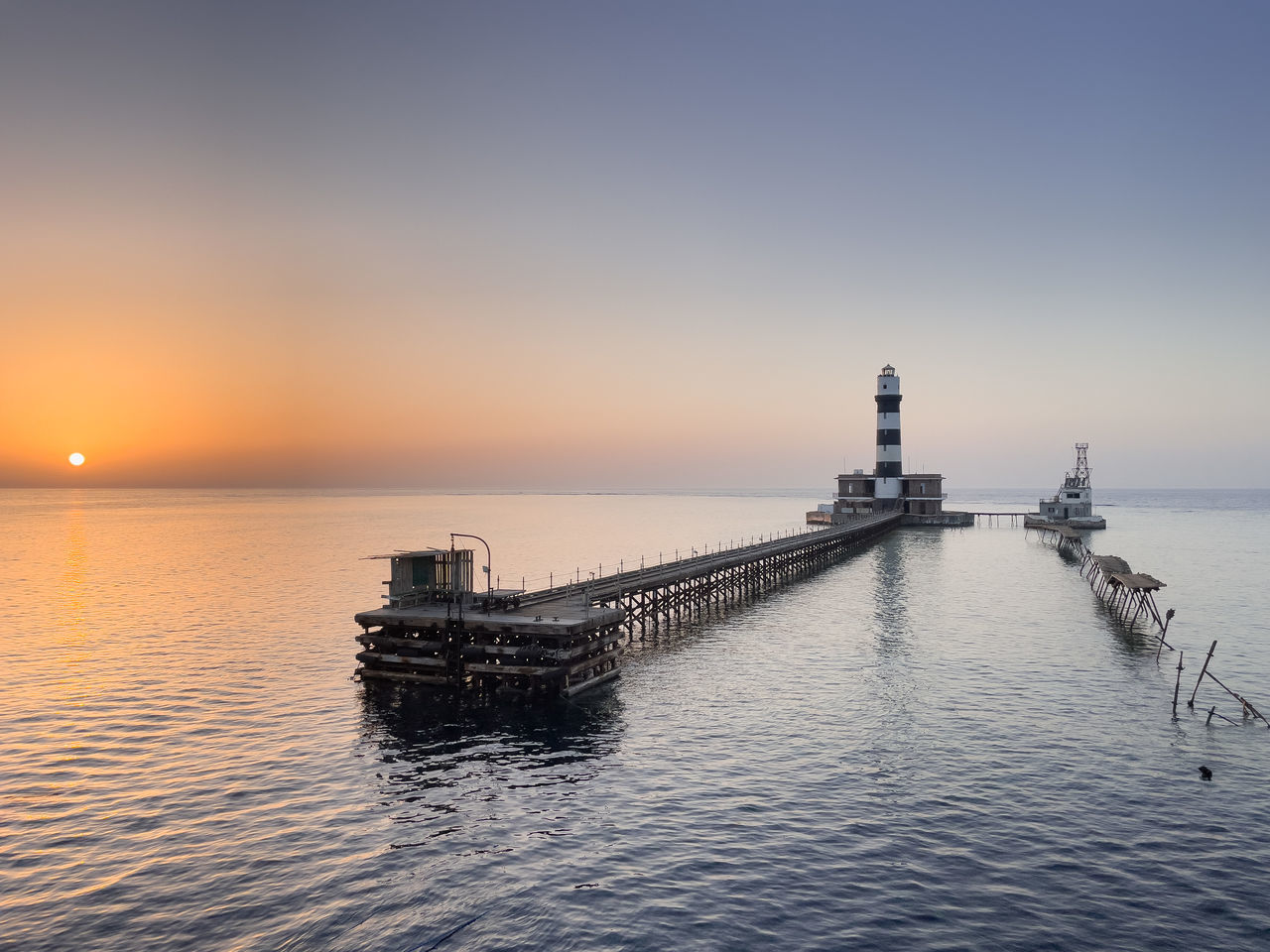 water, sky, sea, lighthouse, sunset, architecture, horizon, nature, transportation, nautical vessel, built structure, scenics - nature, beauty in nature, tranquility, horizon over water, travel, ocean, dusk, travel destinations, tranquil scene, vehicle, reflection, tower, no people, guidance, pier, building exterior, outdoors, copy space, idyllic, building, seascape, ship, mode of transportation, channel, sunlight, environment, coast, beach, twilight, silhouette, clear sky, land, bay, sun, evening, urban skyline, shore, landscape, tourism