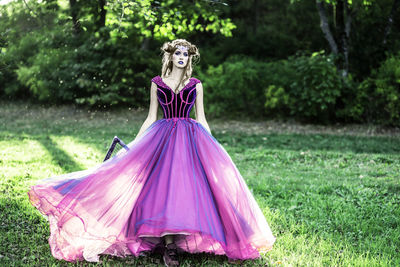 Full length portrait of young woman wearing evening gown standing on grassy field