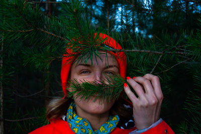 Portrait of woman holding plant against trees