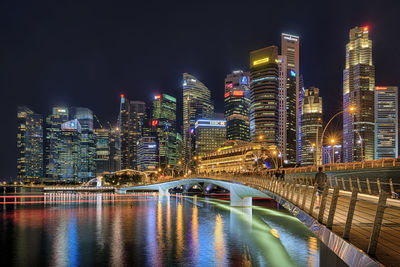 Illuminated buildings by river against sky at night