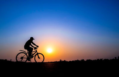 Silhouette man riding bicycle against sky during sunset