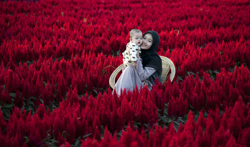 Mom and daughter on red flowering plants on field